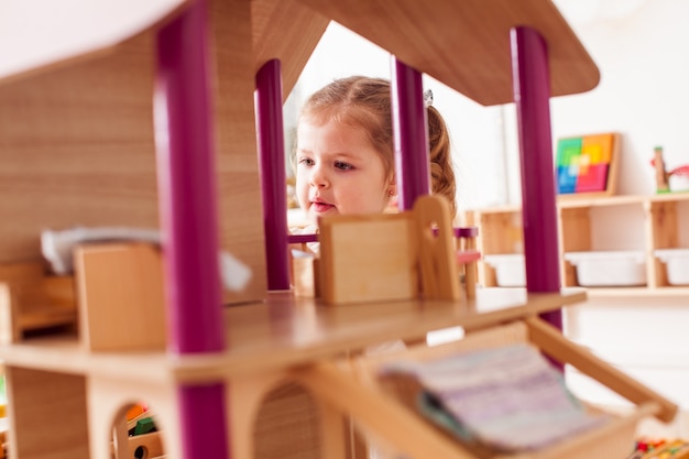 Schönes kleines Mädchen, das mit einem hölzernen Puppenhaus spielt