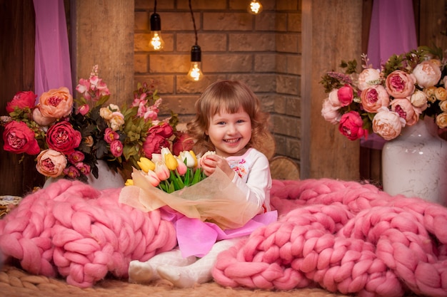 Schönes kleines Mädchen, das mit einer Merinowolldecke mit Blumen in ihren Händen sitzt