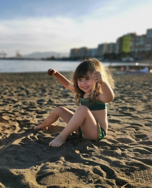 Schönes kleines Mädchen, das mit Sand am Strand spielt