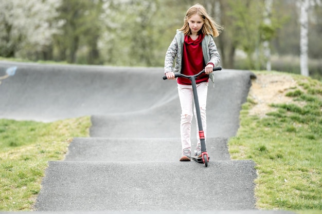 Schönes kleines Mädchen fährt einen Roller in einem extremen Fahrpark