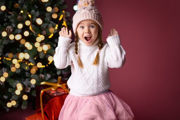 Schönes kleines Mädchen im Hut überraschend nahe Geschenken und im Weihnachtsbaum