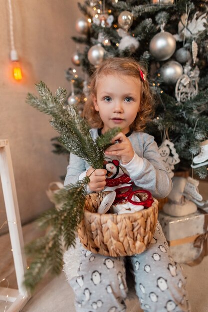 Schönes kleines Mädchen im modischen Pyjama mit einem Zweig des Weihnachtsbaums