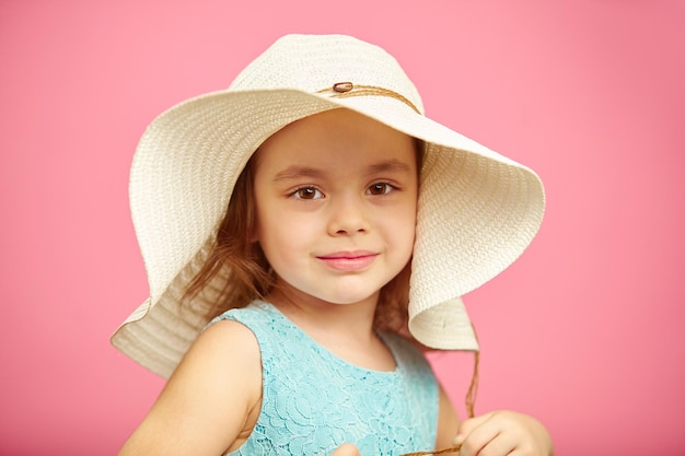 Schönes kleines Mädchen im Strandhut steht über rosa isoliertem Hintergrund