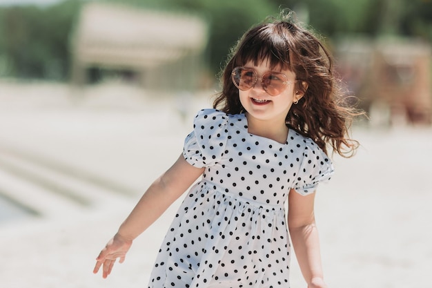 schönes kleines Mädchen im weißen Kleid, das am Strand spielt