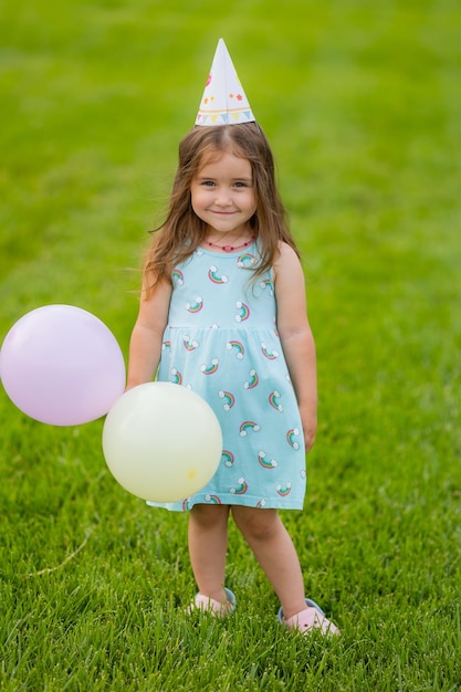 Schönes kleines Mädchen in blauem Kleid und Hut mit Luftballons im Park alles Gute zum Geburtstag