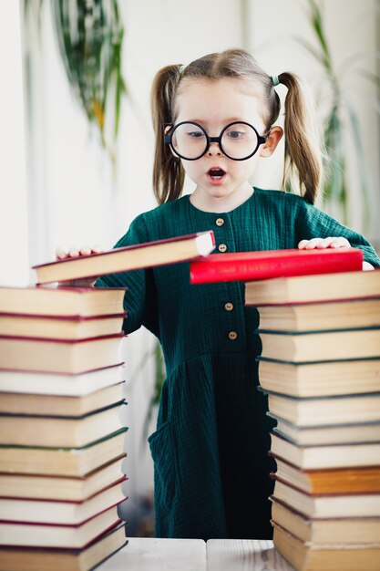 Schönes kleines Mädchen in Gläsern mit Bücherstapel, vertikal