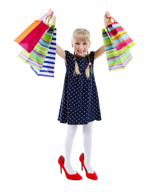 Schönes kleines Mädchen in Mamas Schuhen mit Einkaufstüten lokalisiert auf Weiß