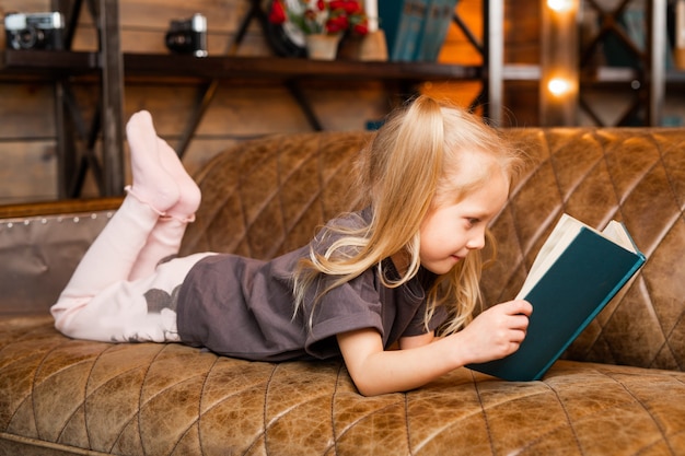 Schönes kleines Mädchen liegt mit einem Buch auf dem Sofa