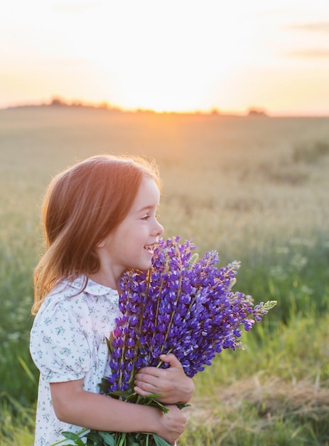 Schönes kleines Mädchen mit Blumenstrauß bei Sonnenuntergang