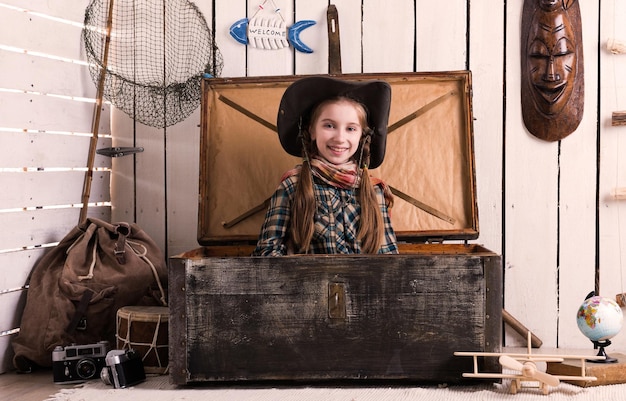 Schönes kleines Mädchen mit Cowboyhut, das in einer Holztruhe sitzt