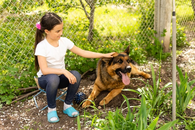 Schönes kleines Mädchen mit einem deutschen Schäferhund, der tagsüber auf dem Rasen spielt.