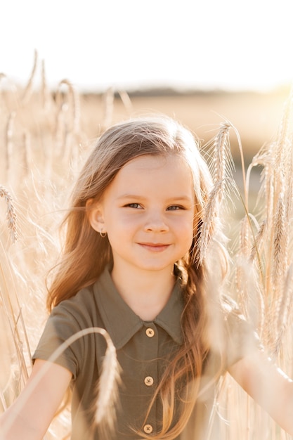 Schönes kleines Mädchen mit langen Haaren, das an einem sonnigen Tag durch ein Weizenfeld geht. Porträt im Freien. Kinder entspannen