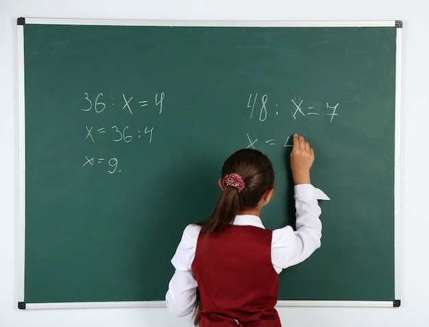 Schönes kleines Mädchen schreibt auf Tafel im Klassenzimmer