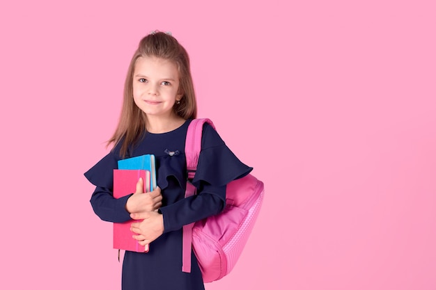 Schönes kluges Mädchen mit Notizbuch, das Schuluniformkleid und rosa hellen Rucksack trägt