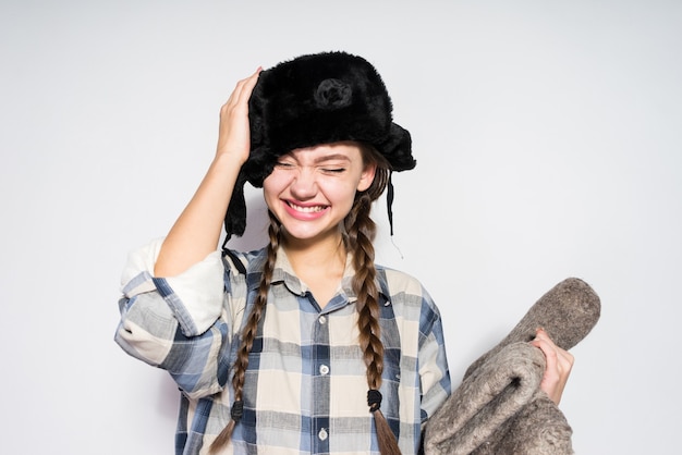 Schönes lachendes Mädchen aus Russland in einer warmen Pelzmütze hält graue Winterstiefel