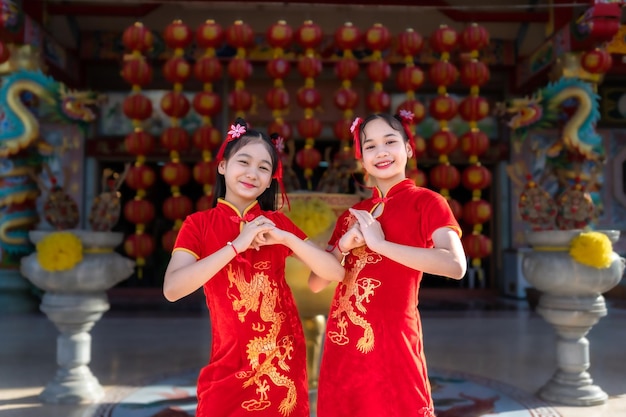 Schönes lächeln des porträts süße kleine asiatin zwei mädchen mit roter traditioneller chinesischer cheongsam-dekoration für das chinesische neujahrsfest am chinesischen schrein
