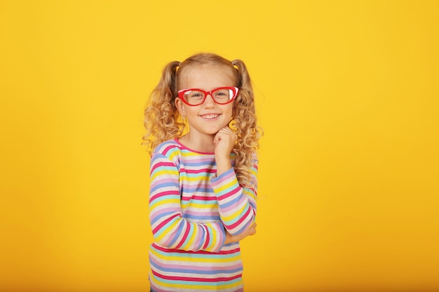 schönes lächelndes blondes Mädchen mit Brille auf gelbem Hintergrund in einer farbigen Jacke Emotionen