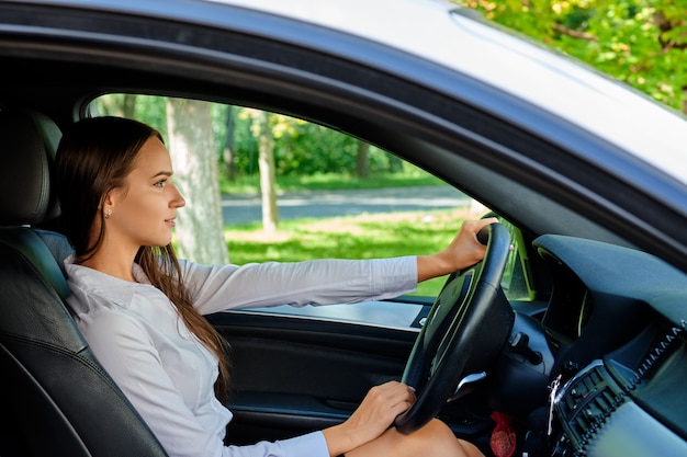 Schönes lächelndes Brunettemädchen hinter dem Steuer eines Autos