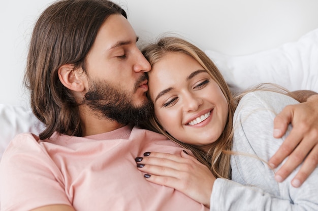 Schönes lächelndes junges Paar, das zu Hause im Bett liegt und sich umarmt
