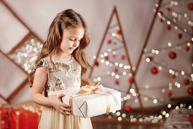 Schönes lächelndes kleines Mädchen, das eine Weihnachtsgeschenkbox hält