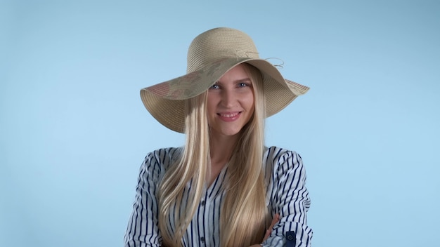 Schönes lächelndes Mädchen, das einen Hut auf ihren Kopf auf blauem Hintergrund setzt
