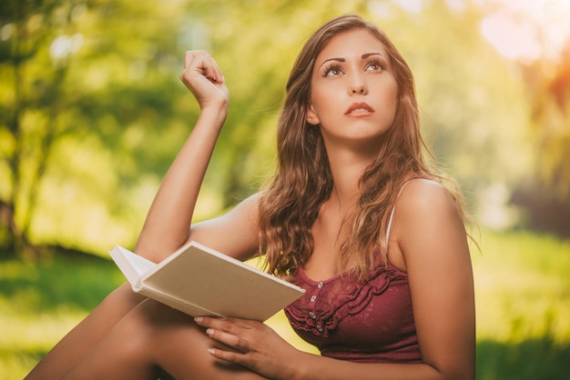 Schönes lächelndes Mädchen liest Buch im Park und denkt.