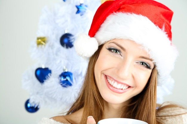 Schönes lächelndes Mädchen nahe Weihnachtsbaum mit Tasse