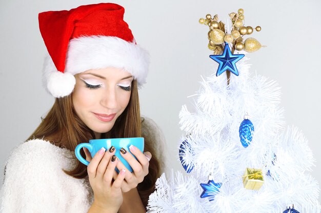 Schönes lächelndes Mädchen nahe Weihnachtsbaum mit Tasse