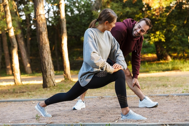 Schönes lächelndes Paar in Sportkleidung, das Übungen beim Training im grünen Park an sonnigen Sommertagen macht