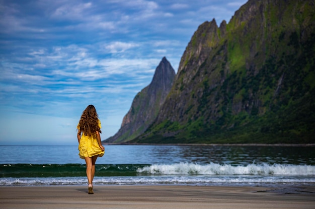 schönes langhaariges mädchen im gelben kleid geht am berühmten strand ersfjordstranda, senja, norwegen spazieren