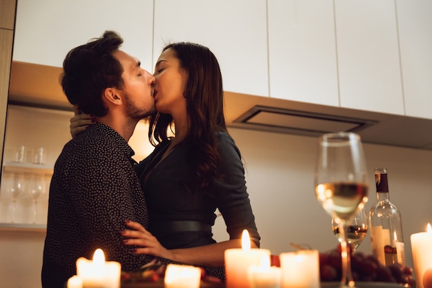 Schönes leidenschaftliches Paar, das ein romantisches Abendessen bei Kerzenlicht zu Hause hat und küsst