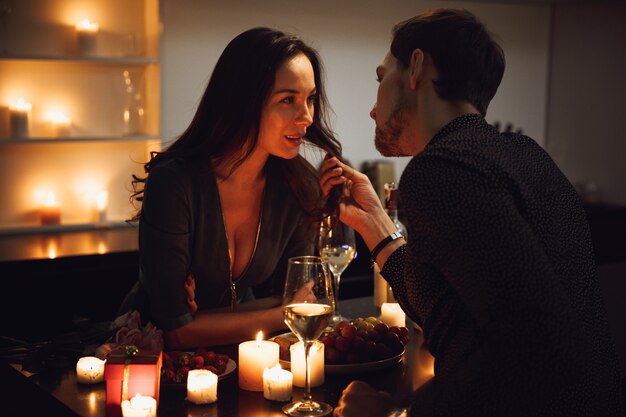 Schönes leidenschaftliches Paar, das ein romantisches Abendessen bei Kerzenlicht zu Hause hat, Wein trinkt, röstet, umarmt