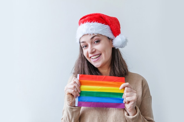 Schönes lesbisches Mädchen im roten Weihnachtsmannhut mit LGBT-Regenbogenfahne lokalisiert auf weißem Hintergrund