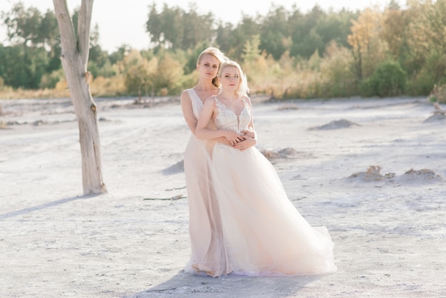 Schönes lesbisches Paar, das auf Sand entlang eines Flussufers an ihrem Hochzeitstag geht