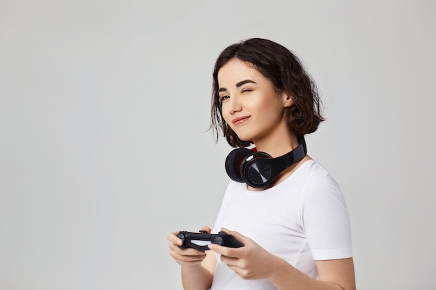 Schönes lockiges Mädchen, das Videospiele auf der Konsole auf grauem Hintergrund spielt