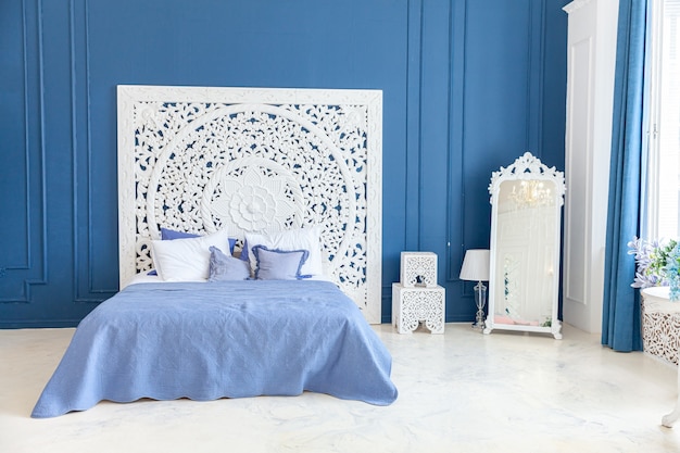 Schönes luxuriöses, klassisches, sauberes Innenschlafzimmer in weißer und tiefblauer Farbe mit Kingsize-Bett und schicken geschnitzten Möbeln. Helles, modernes, stilvolles Innenschlafzimmer und Wohnzimmer im minimalistischen Stil.