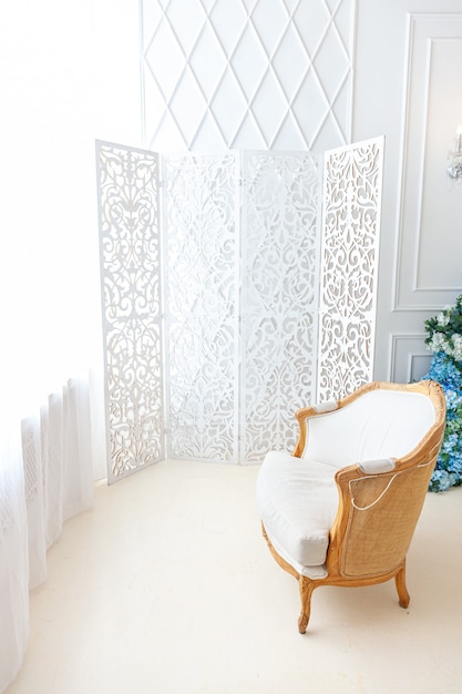 Schönes luxuriöses klassisches weißes, helles, sauberes Innenschlafzimmer im Barockstil mit großem Fenster, Sessel und Blumenkomposition.