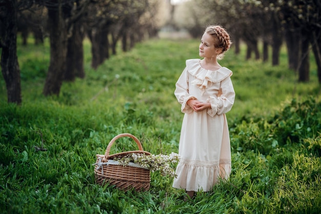 Schönes Mädchen 6-7 Jahre alt, das im Garten im weißen Kleid aufwirft. Osterzeit. genießt Frühling und Wärme. Glückliche Kindheit, Frieden und Glück Konzept. Aromatische Blüte und Retro Vintage.