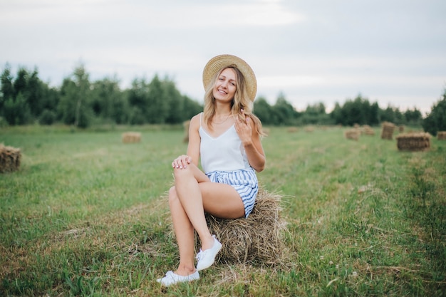 schönes Mädchen auf dem Feld. Frau und Heuballen. blond in einem strohhut. Leben im Dorf