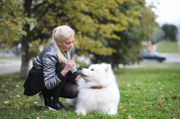 Schönes Mädchen auf einem Spaziergang mit einem schönen flauschigen Hund SamoyedxA