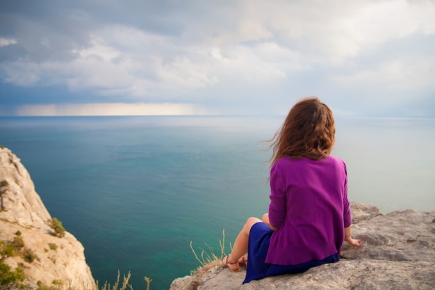 Schönes Mädchen, das auf Felsen sitzt und Meer betrachtet