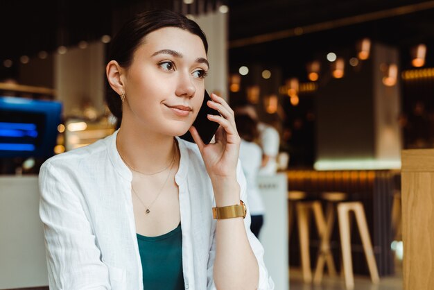 schönes Mädchen, das auf Smartphone im Café spricht