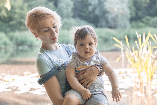 Foto schönes mädchen, das ein kind in ihren armen auf dem hintergrund des sees hält