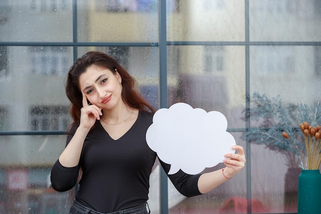 Schönes Mädchen, das eine Ideenblase in Wolkenform hält und sich beim Denken den Finger an den Kopf legt