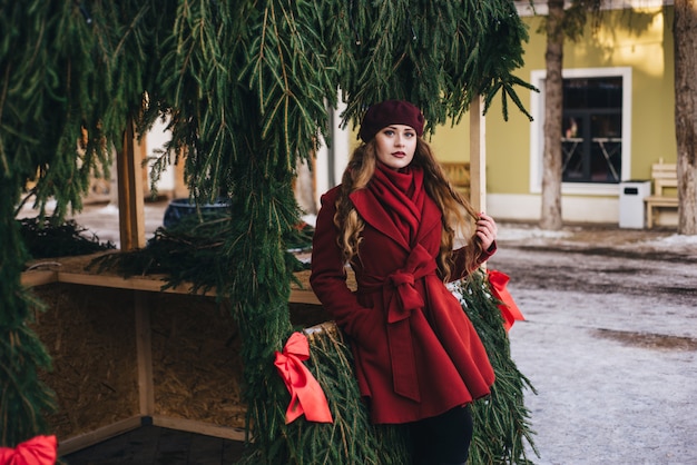 Schönes Mädchen, das einen roten Mantel und ein Barett auf Weihnachtsstraße trägt