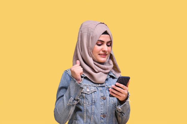 schönes Mädchen, das Hijab mit Denim-Jeans trägt, glücklich und mit dem indischen pakistanischen Telefonmodell