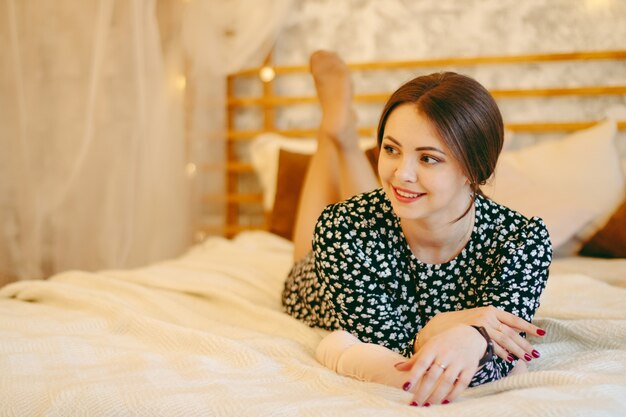 Schönes Mädchen, das im Bett auf ihrem Bauch liegt, Mädchen in einem Kleid