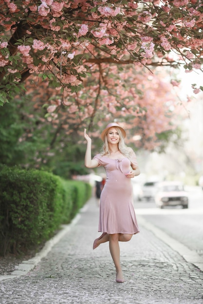 Schönes Mädchen, das im blühenden Garten der rosa Pfirsich- und Sakura-Blumen aufwirft. Junge attraktive Frau lächelnd, im Freien posierend. Frühling, Schönheitskonzept.