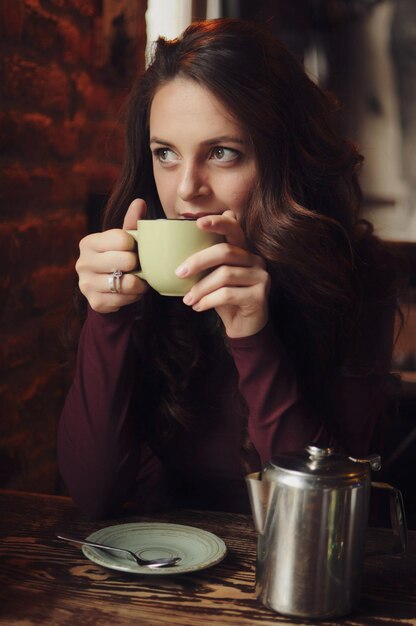 Schönes Mädchen, das im Café sitzt, trinkt Kaffee und schaut auf das Fenster Warmes, gemütliches Porträt