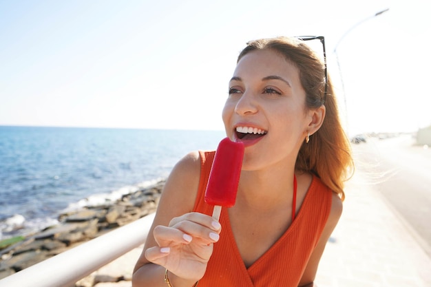 Schönes Mädchen, das im Sommer ein rotes Eis am Strand der Promenade isst